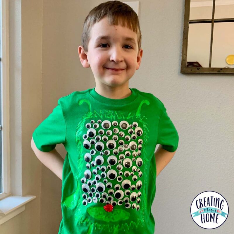 A little boy wears a green shirt that has googly eyes on it.