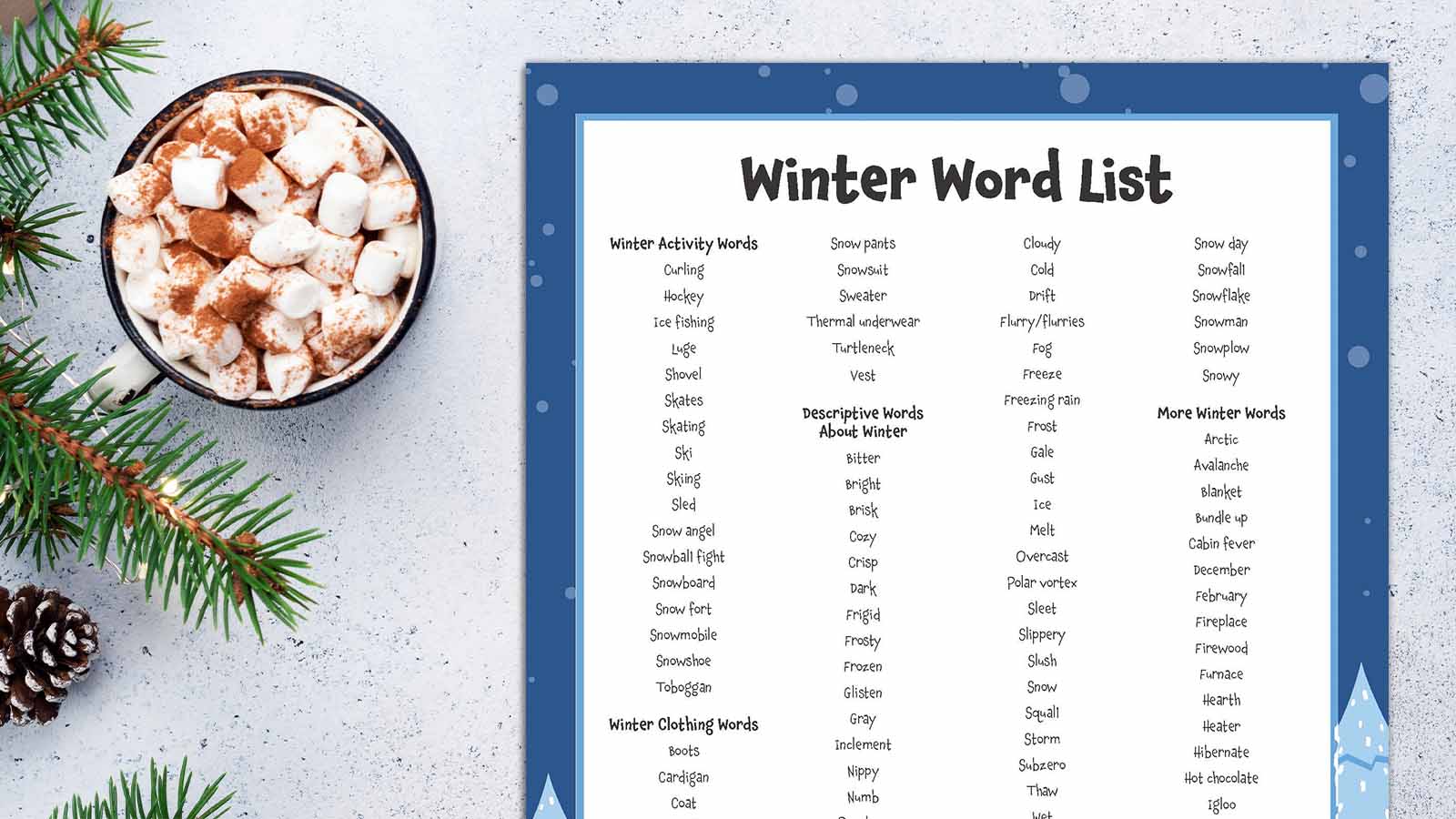 Winter words printable sheet next to a sprig of greenery and a mug of hot cocoa with marshmallows.